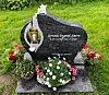 Gravstein med navnet Jorunn Ingerd Sætre, blomster, krans og en liten engelfigur i en gresskledd hage.