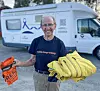 Smilende mann står foran en bobil med en oransje pose og en stor gul sekk.