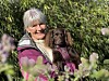 En gråhåret kvinne holder en liten brun hund i en blomstrende hage.