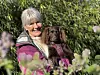 En gråhåret kvinne holder en liten brun hund i en blomstrende hage.