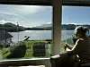 En kvinne sitter ved et vindu og ser ut over en fjord omgitt av fjell.