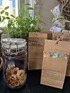Dekorerte papirposer og glass med tørkede råvarer står på et bord ved siden av grønne planter.