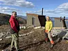 To turgåere står ved en liten hytte i et steinete fjellandskap under blå himmel.