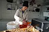 En person i arbeidsklær sorterer oransje bær fra greiner ved siden av en fryseboks.