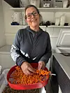 En kvinne sorterer oransje bær i et rødt kar på et lyst arbeidsrom.