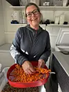 En kvinne håndterer oransje tindvedbær i en rød balje på et arbeidsrom.