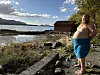 En kvinne med blått håndkle står på en steinete strand ved en fjord.