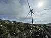 Flere vindturbiner står på et steinete, vegetasjonskledd fjellplatå under en skyet himmel.