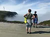 To personer står på en grusvei ved et grønt fjellandskap innhyllet i tåke.