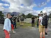 En gruppe mennesker står ved en grusvei under en filminnspilling, med fjell og skyer i bakgrunnen.