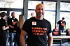 Smilende mann i svart T-skjorte står foran flere personer i et lyst lokale.