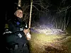 Uniformert tjenesteperson med lommelykt i en mørk skog.