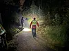 Person i refleksklær går på en opplyst skogssti om natten.