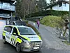 Norsk politibil parkert ved boliger, med en person på en sti i bakgrunnen.