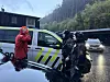 Personer står ved et hvitt utrykningskjøretøy på en regnvåt vei omgitt av skog.