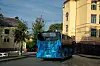 Blå buss på en bygate foran en gul historisk bygning.