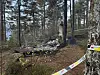 Avsperret skogsområde med et ødelagt kjøretøy og vrakdeler mellom trærne.