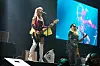 To musikere opptrer på en konsertscene med gitarer og en stor videoskjerm.