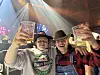 To personer i cowboyhatter skåler med ølglass foran scenen.