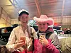 To smilende kvinner med cowboyhatter holder drikke i et innendørs lokale.