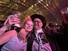 To personer poserer under fargerike lys; den ene holder et glass, og den andre bruker cowboyhatt.