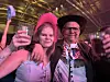 To festdeltakere poserer sammen i rosa og lilla lys foran en scene.