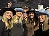 Fem kvinner i cowboyhatter smiler sammen under et innendørs arrangement.