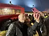 Mann tar selfie med kvinne foran et rødt utrykningskjøretøy innendørs.