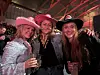 Tre kvinner i cowboyhatter smiler og holder drinker på en fest.