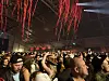 Tett folkemengde på konsert i en hall med røde dekorasjoner og scenelys.