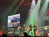 Band spiller på en opplyst scene foran et stort lerret med konsertbilder.