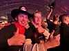 Smilende mann i cowboyhatt viser tommelen opp i en folkemengde under rosa scenelys.