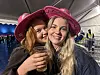 To smilende kvinner i rosa hatter, hvor den ene holder et glass, i et festtelt.