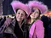 To smilende kvinner i rosa cowboyhatter poserer foran en folkemengde om kvelden.