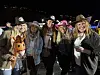 En gruppe venner i hatter og festklær poserer utendørs om kvelden.