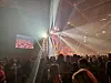 Konsertpublikum foran en scene med sterke lysstråler og videoskjermer.