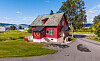Tradisjonelt rødt trehus ved en vei i et grønt, landlig landskap.