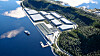 Flyfoto av et stort industrikompleks ved en skogkledd fjord med brygge og båt.
