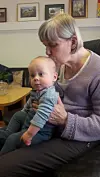 Voksen person holder en baby på fanget i en stue med bilder på veggen.
