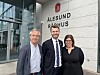 Tre personer foran Ålesund rådhus med kommunevåpen og skilt på fasaden.