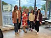 Gruppe voksne samlet ved et stort vindu i et lyst lokale med utsikt mot vannet.