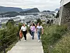 Tre personer går opp en trapp med utsikt over en havn, by og fjell.