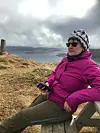 Kvinne i rosa jakke sitter på en benk med utsikt over havet.
