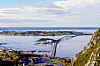 Utsikt over fjord, kystbebyggelse og en lang bro fra en bratt fjellside. Giske.