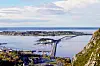 Utsikt over fjord, kystbebyggelse og en lang bro fra en bratt fjellside. Giske.
