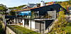 Moderne hus med glassfasade og terrasse i et skogkledd landskap.