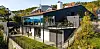 Moderne hus med glassfasade og terrasse i et skogkledd landskap.