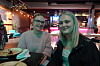 To kvinner smiler ved et restaurantbord med fargerik belysning i bakgrunnen.