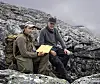 To fotturister sitter i et steinete fjellandskap, med kart og ryggsekker.