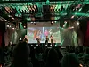 Publikum ser mot en opplyst scene med flere personer og en presentasjon på storskjerm.